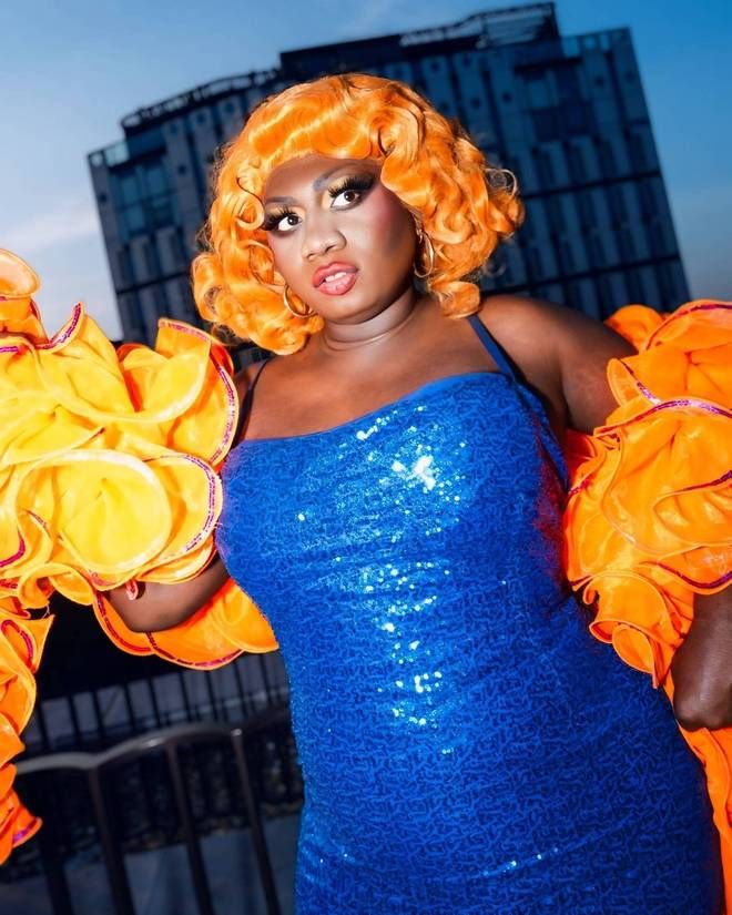 Yshee Black in a blue sequin dress and orange ruffled boa on a rooftop