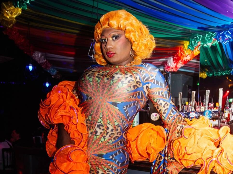Yshee Black performing on stage in orange ruffles under rainbow lights